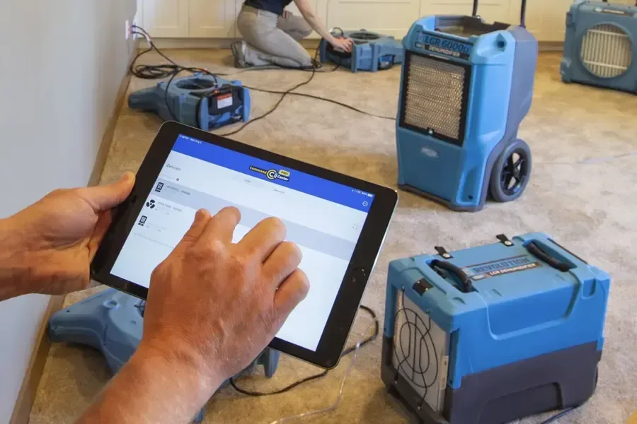 Drying readings logged on a tablet next to running dehumidifiers and air movers