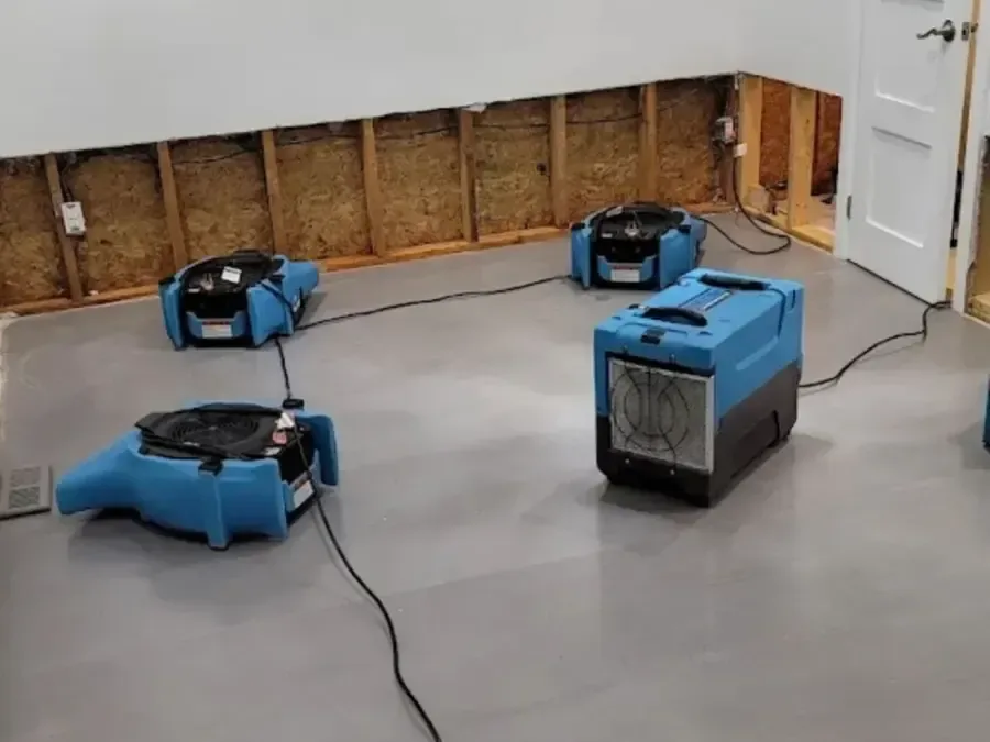A dehumidifier and air movers running in a room with the lower drywall cut away