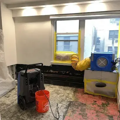 A dehumidifier and an air mover set up in a room where the flooring has been removed during drying