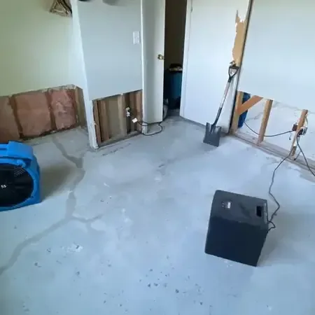 Air movers and a dehumidifier running in a room with the lower drywall cut out and a bare floor