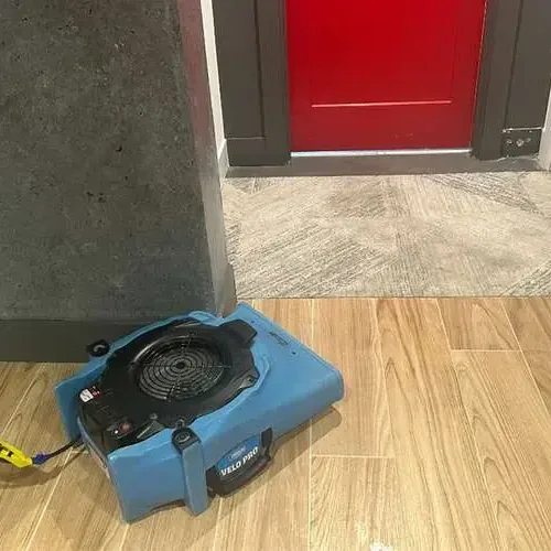 An air mover pushing dry air across a wood-look tile floor beside an open doorway