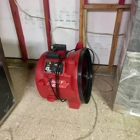 A red air mover beside a lower wall that was opened up, with plastic sheeting hung nearby
